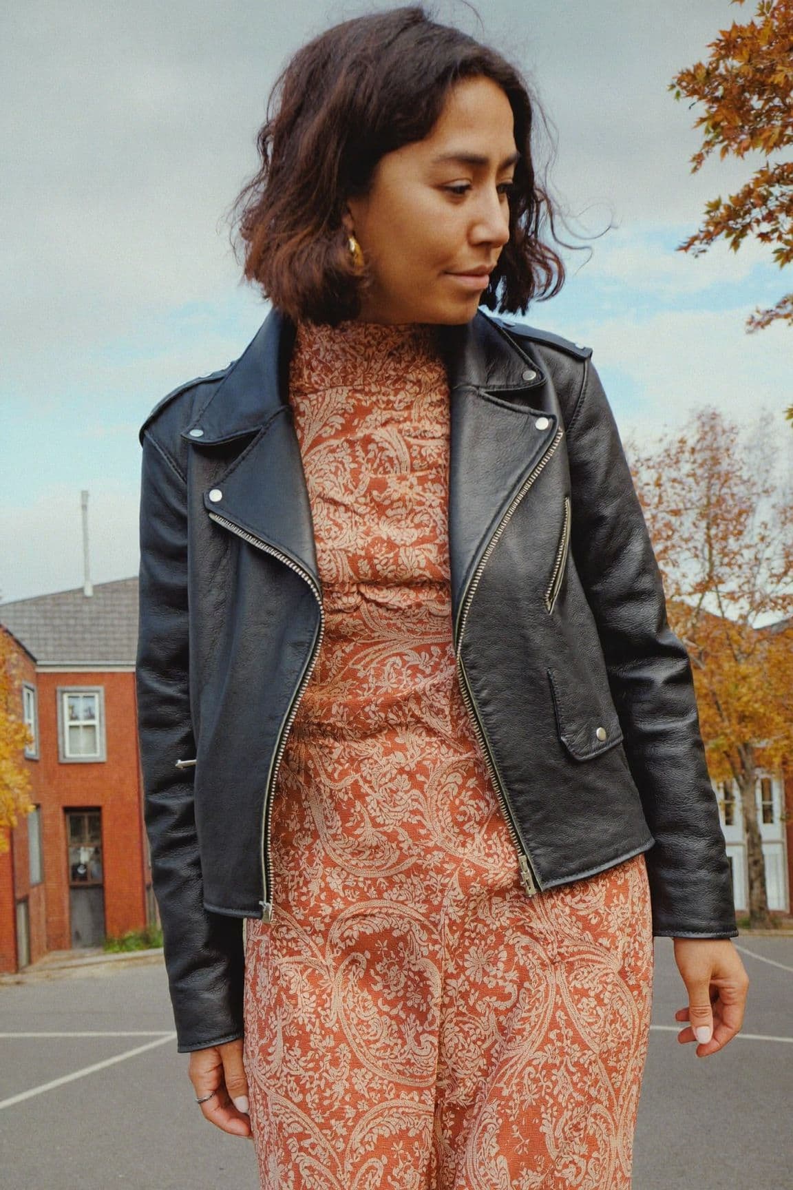 A woman in a rust paisley maxi dress under a black leather biker jacket on a residential street