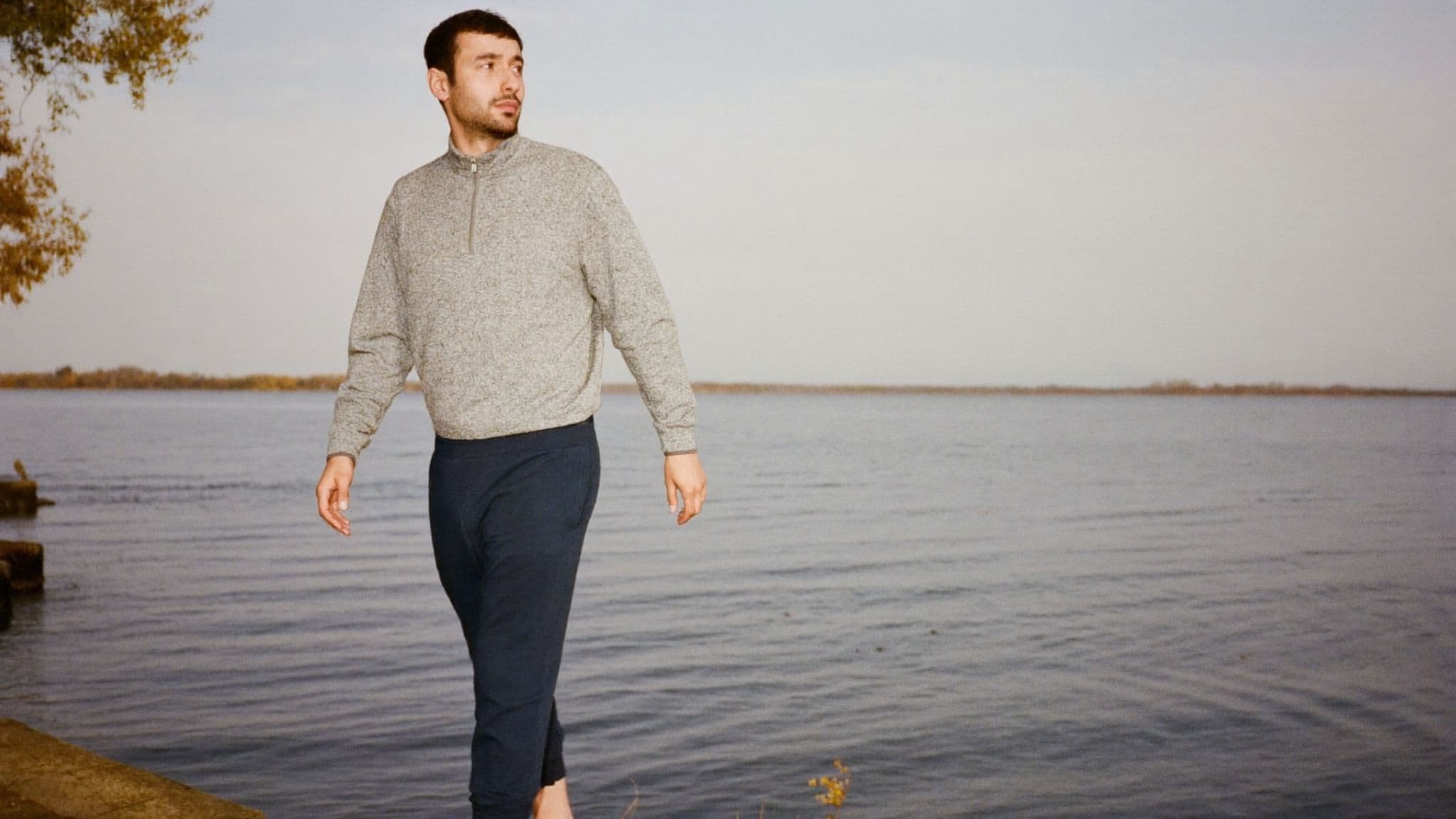 Man in a grey half-zip pullover and navy joggers walking beside a lake