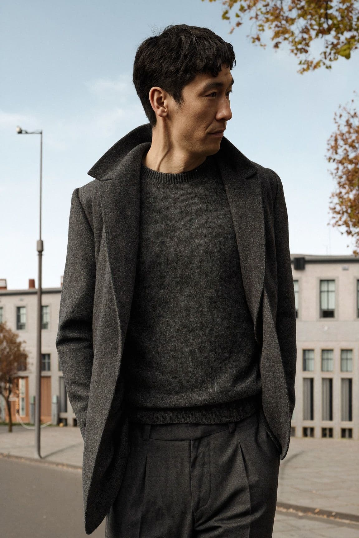 A man in a charcoal suit over a charcoal knit sweater on a stone-paved street