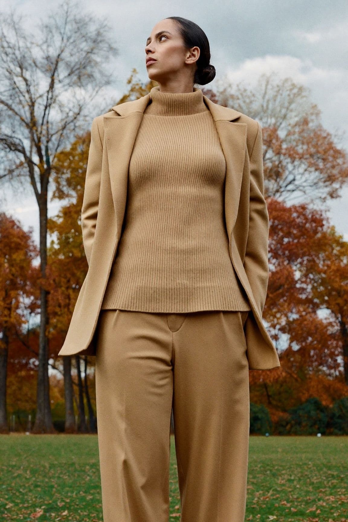 A woman in a camel blazer, camel ribbed knit and camel wide-leg trousers in a park in autumn