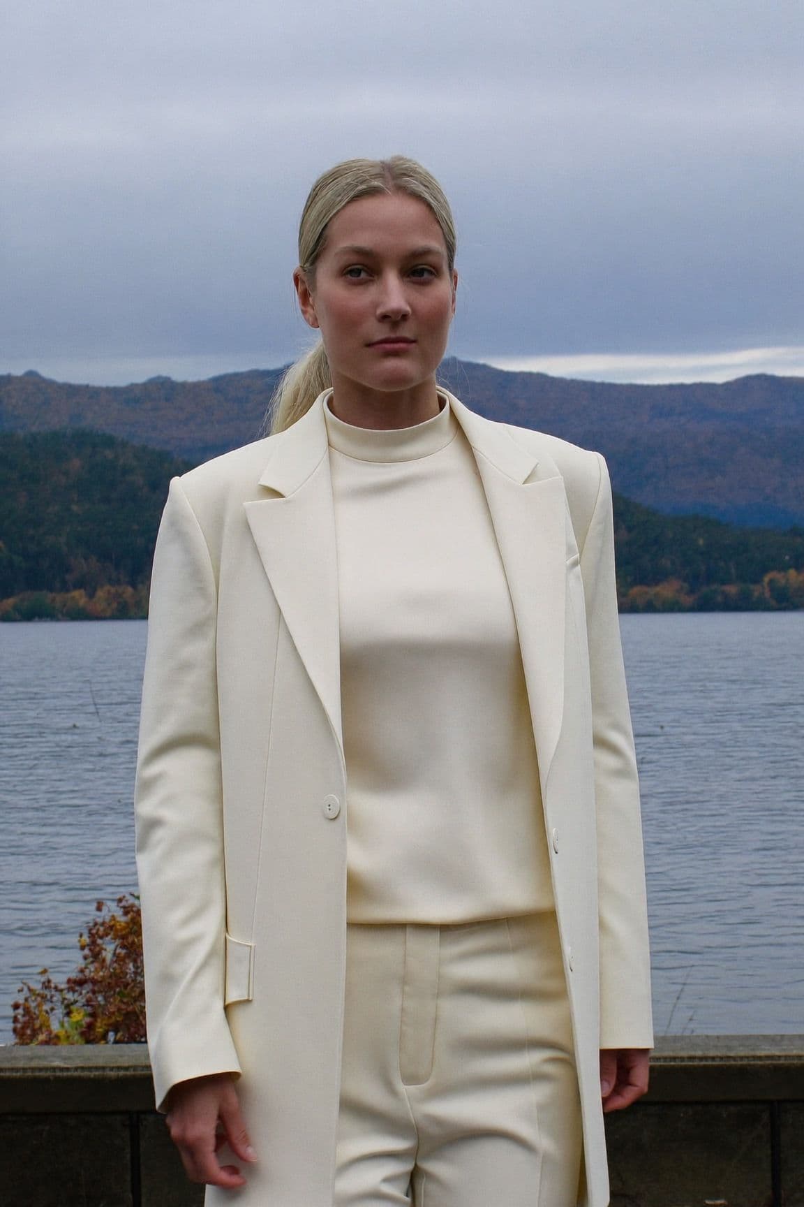 A woman in a head-to-toe cream tailored blazer, silk top and trousers by the water